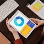 Top view of hands holding a digital tablet displaying a graph in an office setting.